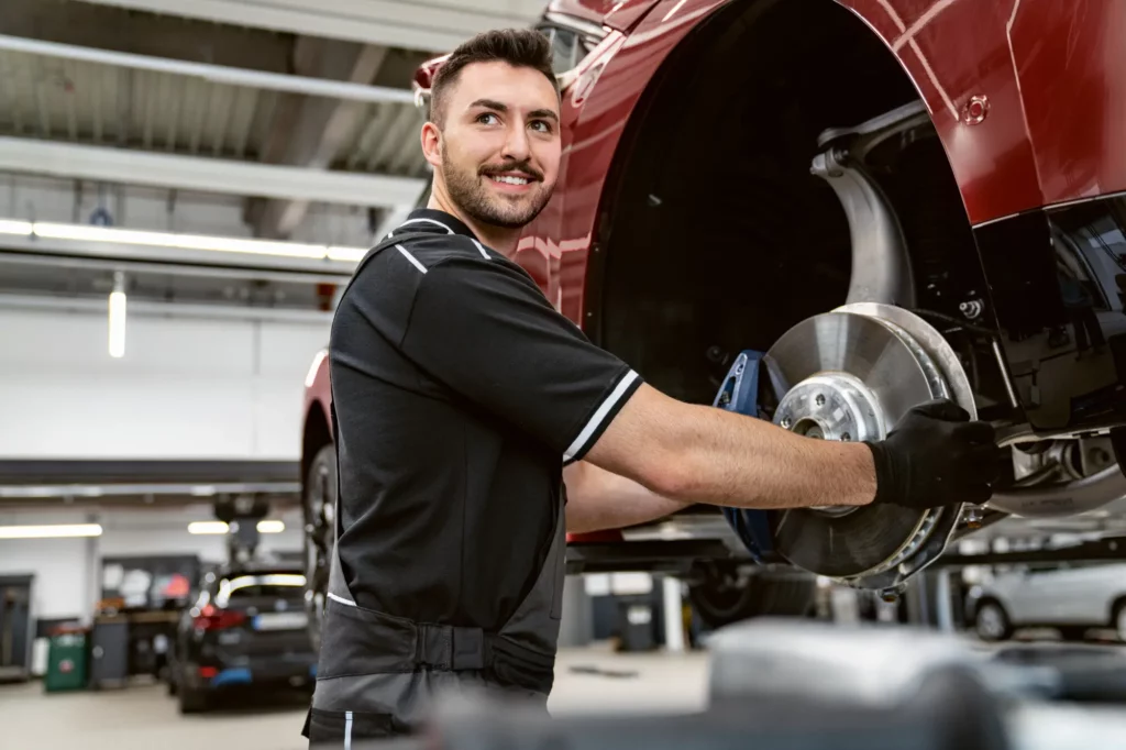 Car mechanics work in the workshop adjusting the wheel axle of a suspended car.