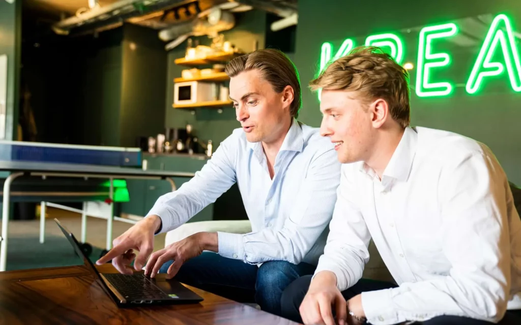 Two men are discussing in Krea's office in front of a laptop and with a ping-pong table in the background.