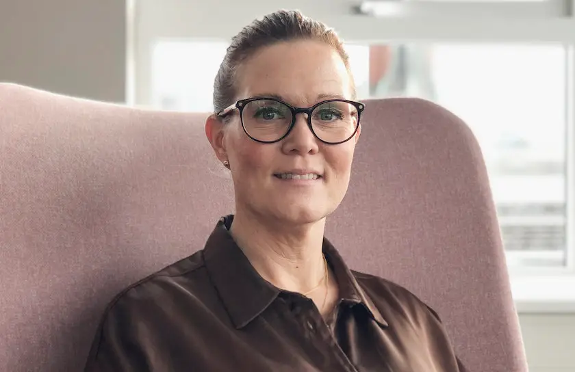 Catherine Borgkvist, Quality Manager at Inyett. Catherine is sitting in an armchair where you can see a small part of the chair. Catherine is wearing a brown shirt and glasses.
